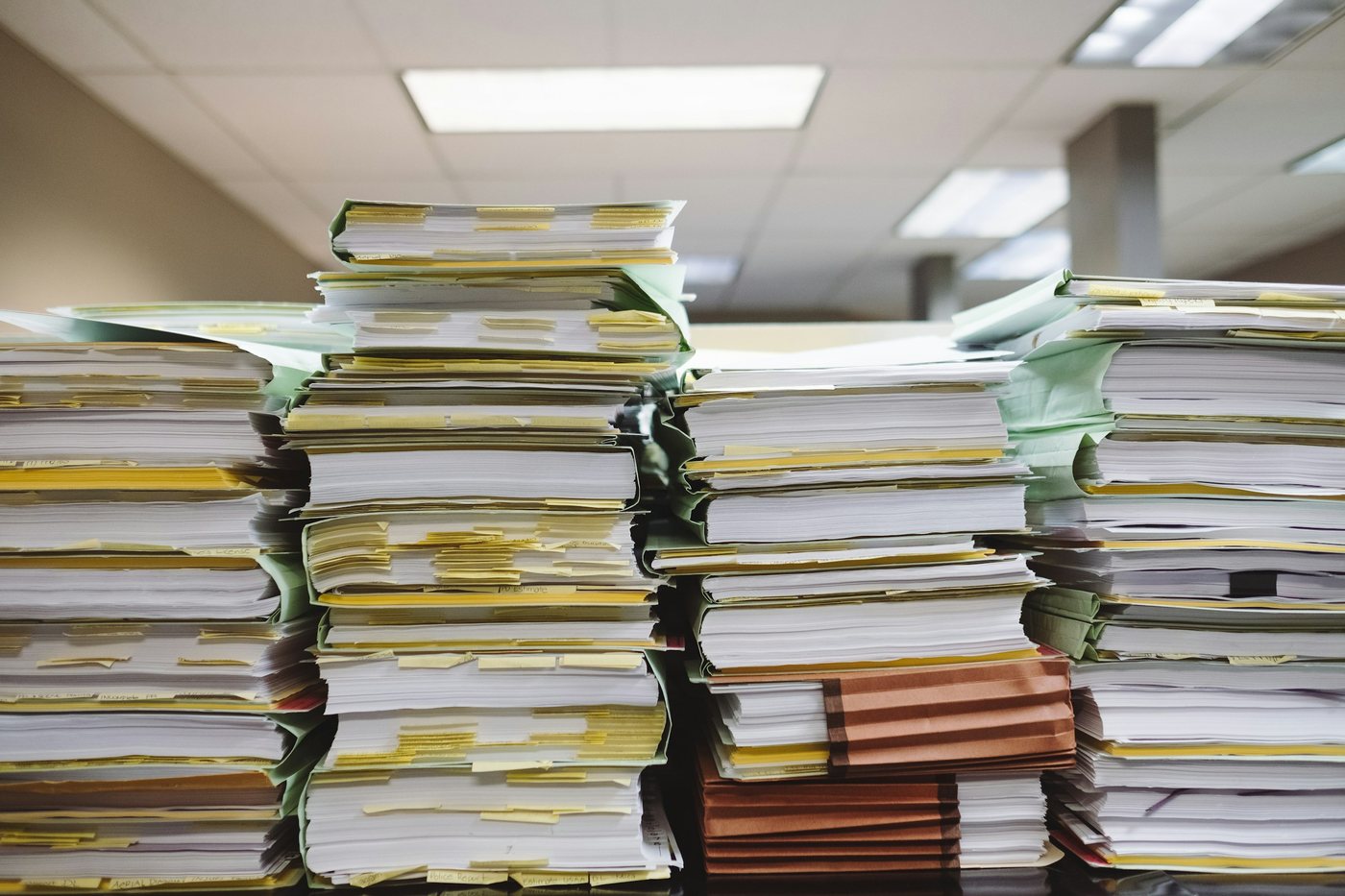 Four tall stacks of bound paper document bundles with index tabs and pale covers, seen edge-on at desk height.